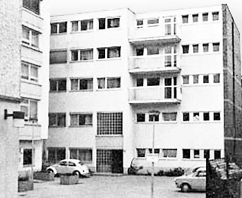 Schwarz-Weiß-Foto eines Hauses mit parkenden Fahrzeugen davor